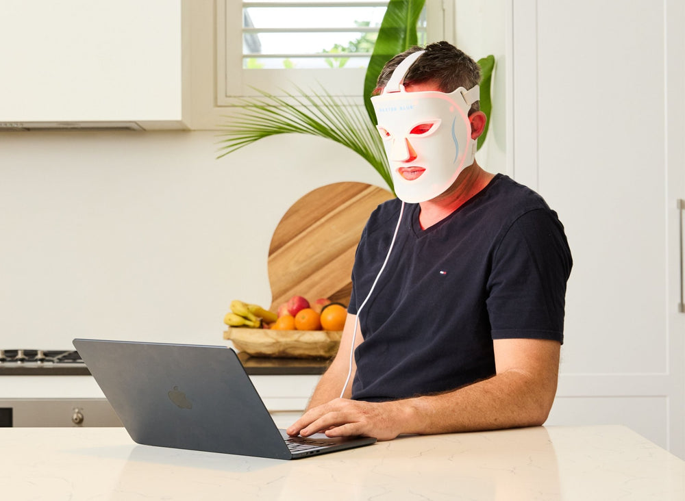 Baxter_Blue_Red_Light_Therapy_Face_Mask_on man using laptop in kitchen