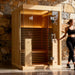 A 2-person indoor infrared sauna in a home setting with a woman standing next to it